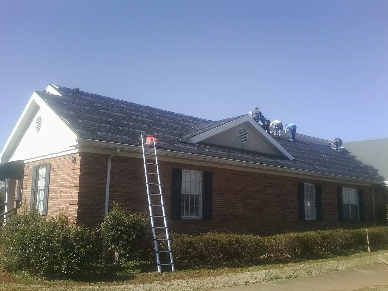 Crew tearing shingles off a brick ranch roof with a ladder set — Emergency Roof Repair work by our crew in Collegeville
