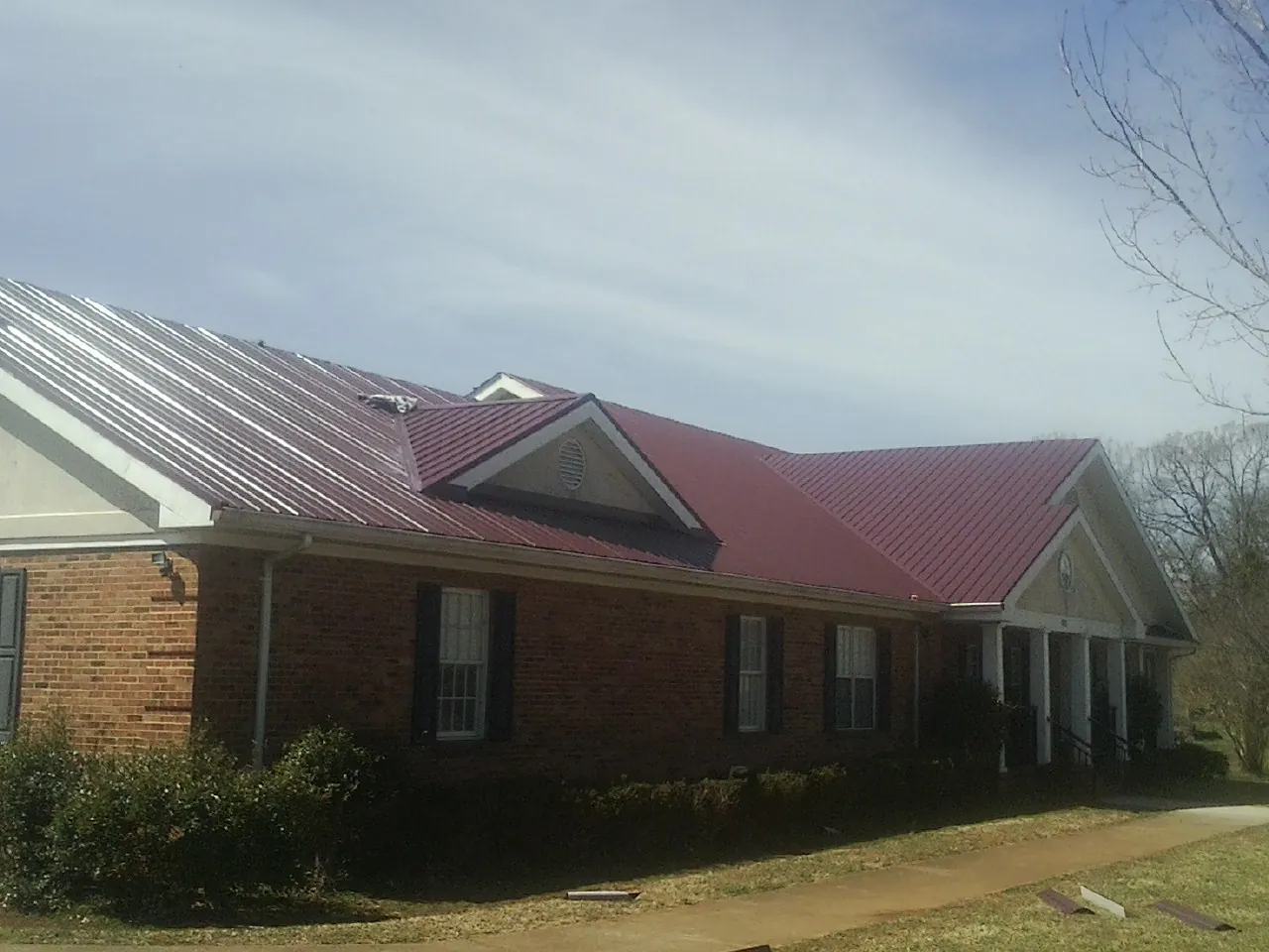 Red metal roof with gabled entries on a long brick building, from a Hail Damage Roof Repair job in Collegeville