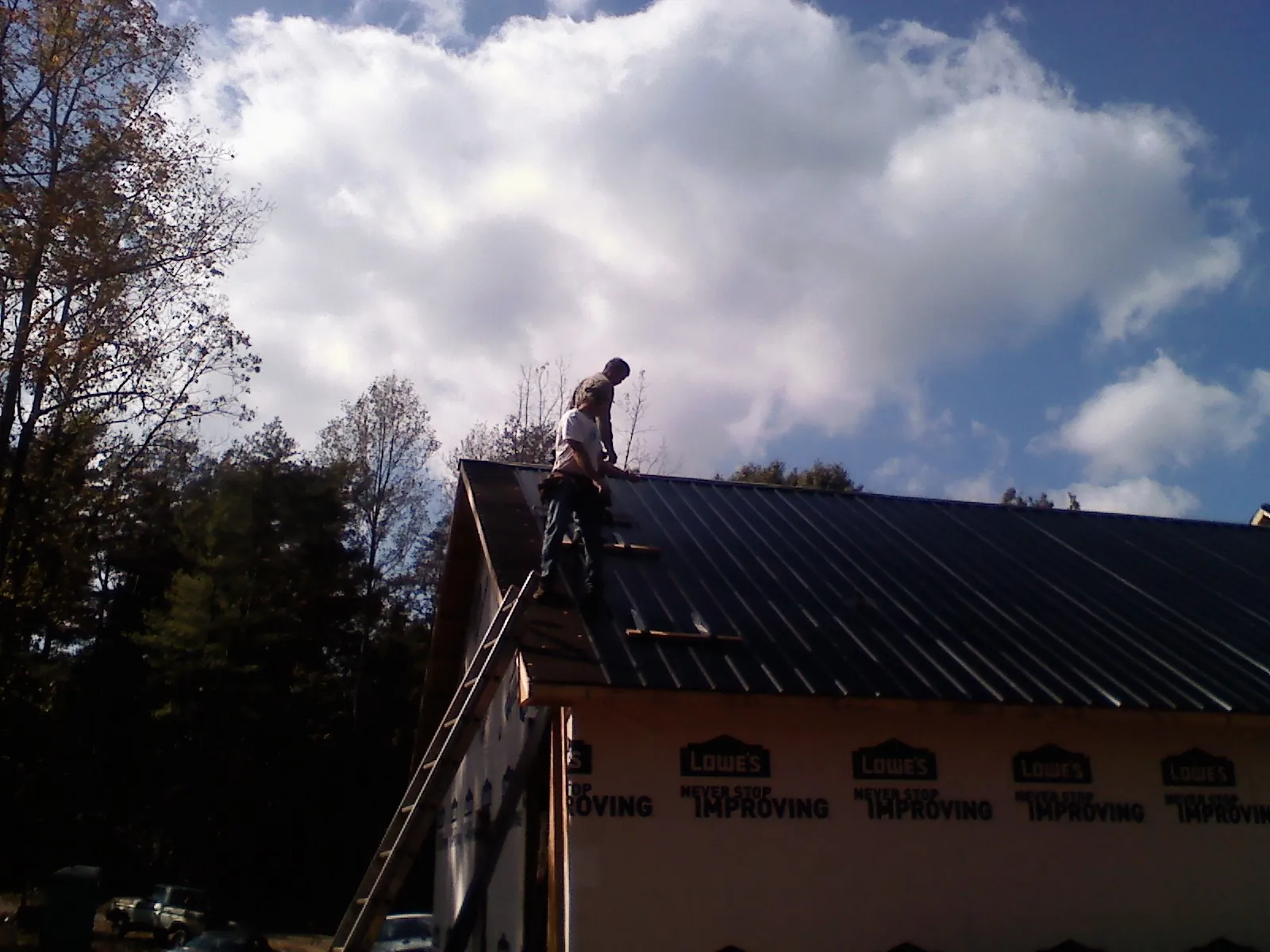Roofer fastening dark metal panels high against a cloudy sky, from a Roof Inspection job in Collegeville
