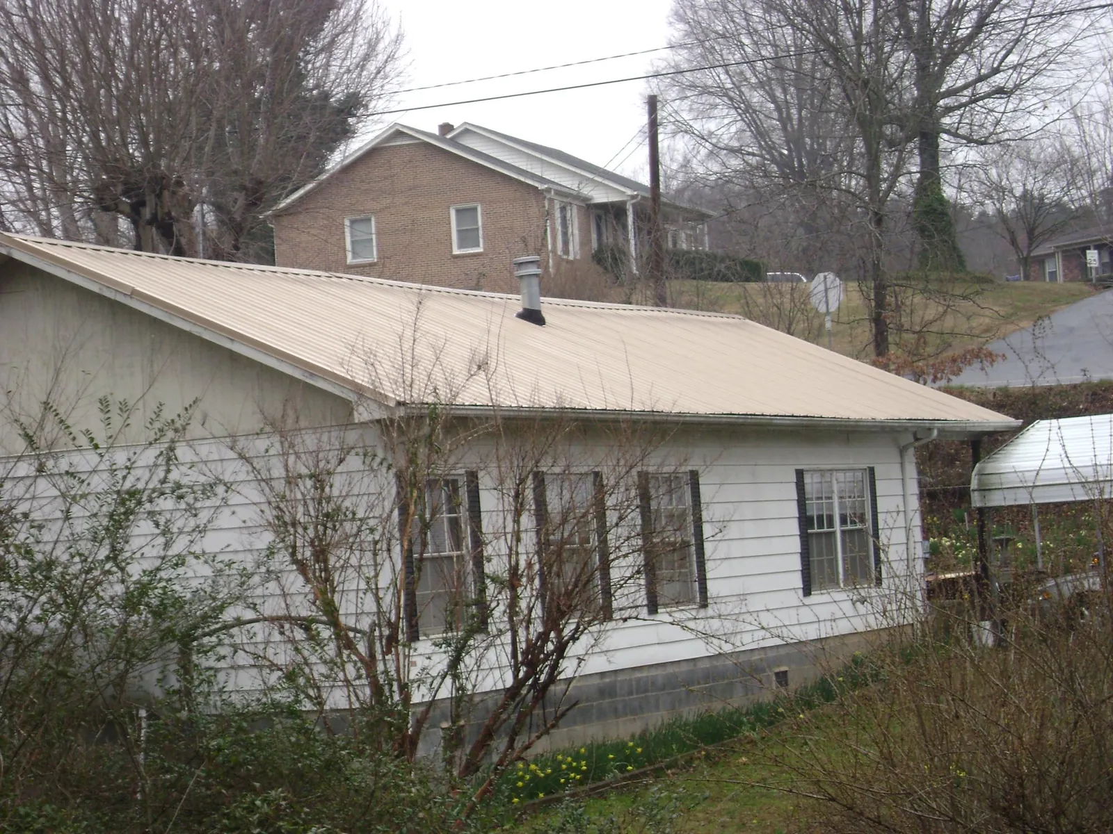 Tan metal roof on a white sided house set into a hillside — Commercial Roofing by Roofing Brothers in Collegeville